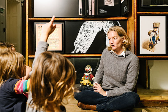 Kinder und eine Frau sitzen vor Regal im Literaturmuseum