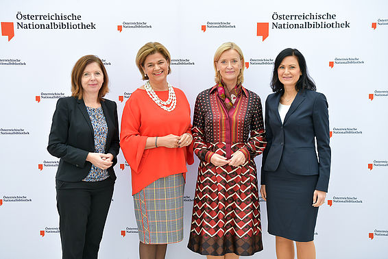 Vier elegant gekleidete Frauen von einer ÖNB-Logowand