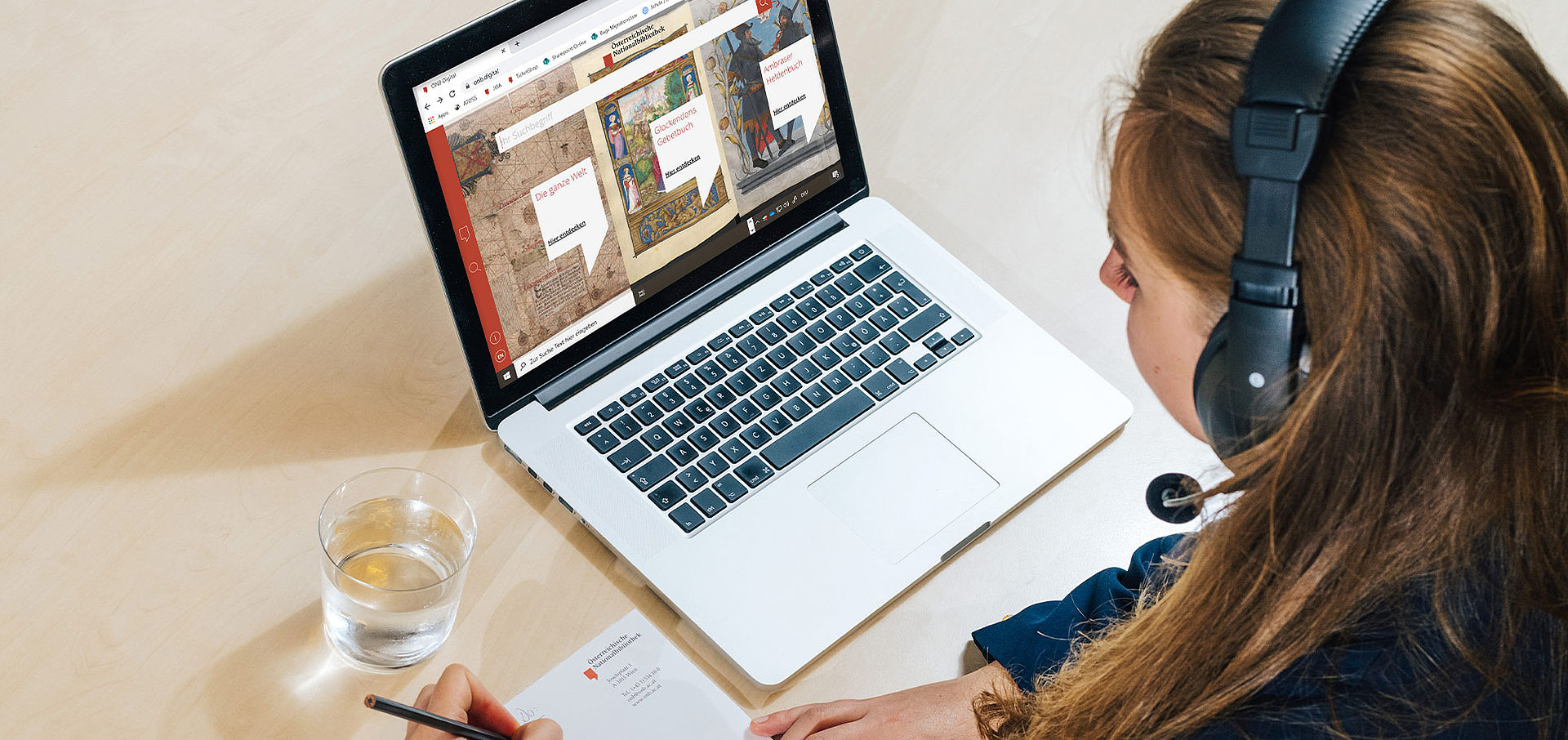 Junge Frau mit Headset sitzt vor Laptop, sie nimmt an einem Webinar teil