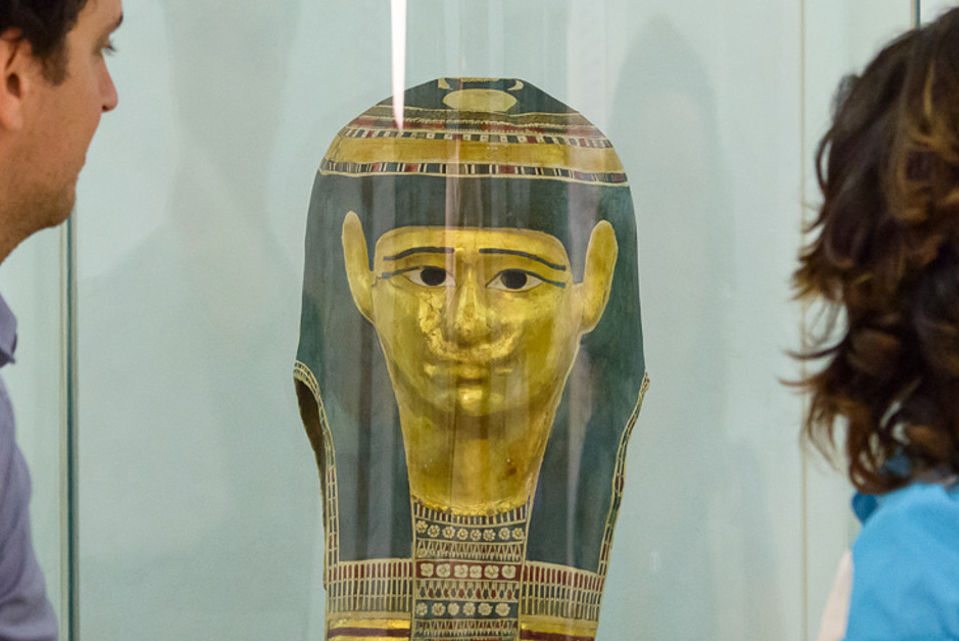 Ein Mann und eine Frau betrachten eine goldene ägyptische Totenmaske im Papyrusmuseum