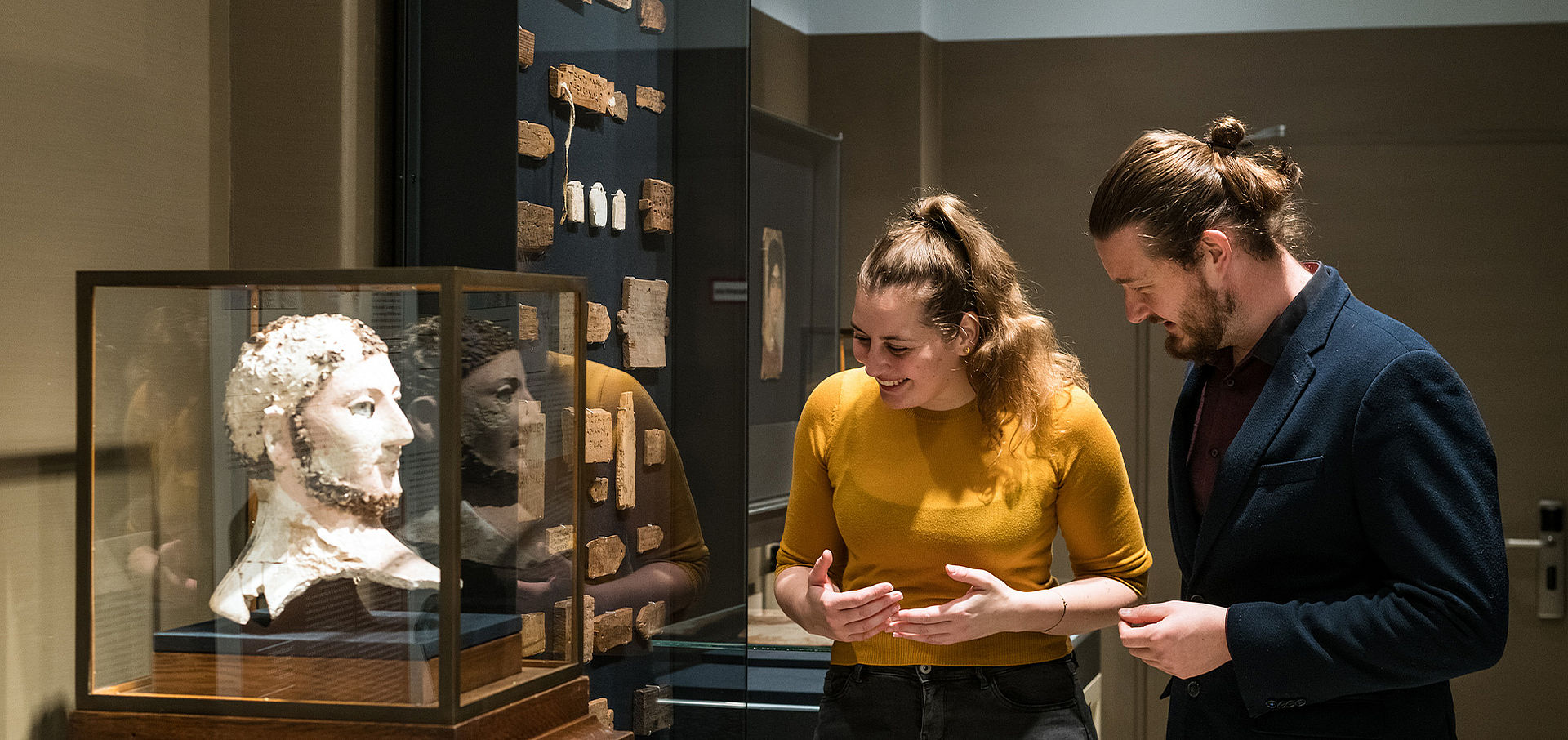 Ein Mann und eine Frau schauen sich eine weiße Büste eines Mannes in einer Vitrine an