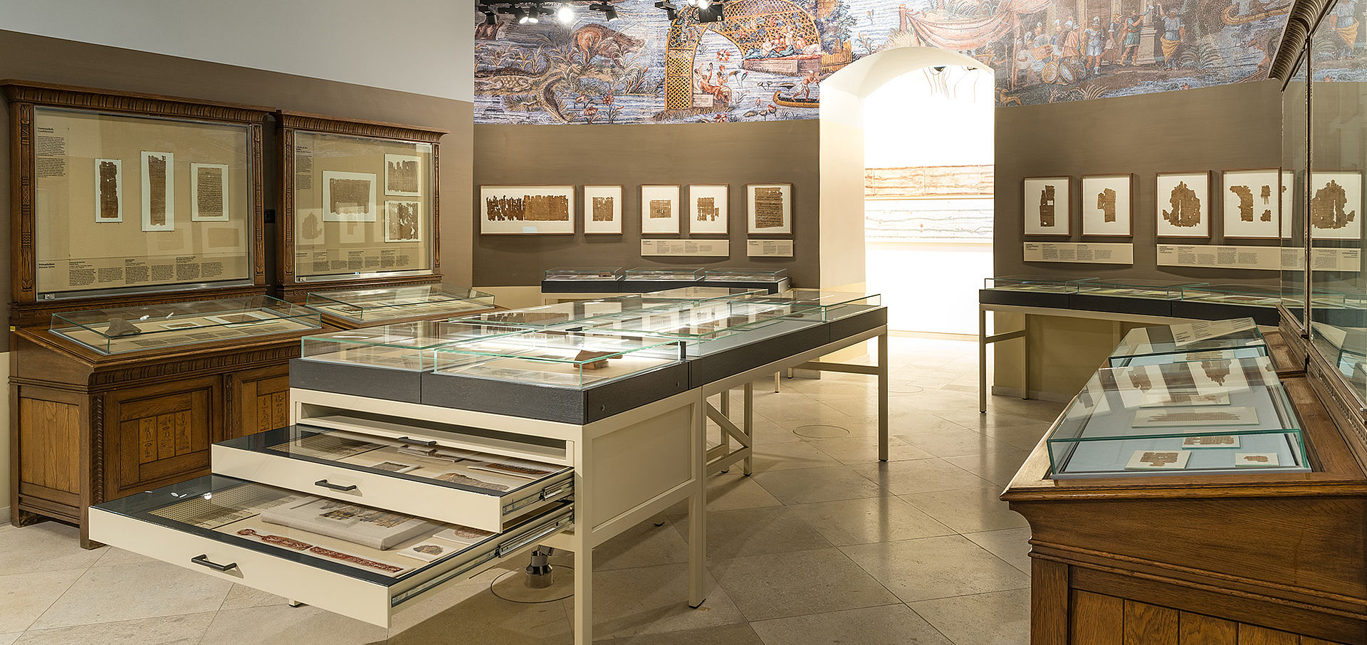 Ansicht des Papyrusmuseums mit vielen Vitrinen und Objekten und buntem Wandgemälde