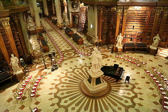 Saal mit Statue und Bücherregalen, am Rand sind Stühle in einer Reihe aufgestellt