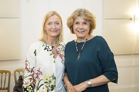 Blonde Frau im Blumenblazer und eine Frau mit blaugrünem Oberteil