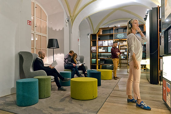 BesucherInnen im Literaturmuseum, eine Frau stehend mit Kopfhörern vor einer Schautafel