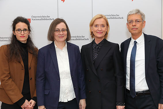 Drei Frauen und ein Mann posieren nebeneinander für ein Foto, im Hintergrund das Logo der Österreichischen Nationalbibliothek.