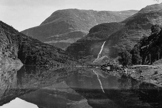 Schwarzweiß-Fotografie einer Landschaft mit Bergen, die sich in einem See spiegeln. 