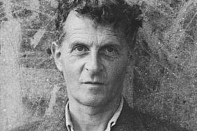 Schwarzweiß-Portrait von Ludwig Wittgenstein vor einer bemalten Mauer