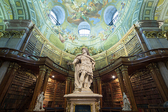 Foto aufschauend zu Deckenfresko und Statue, im Hintergrund Bücherregale
