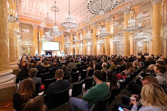 Volles Publikum in einem Marmorsaal von hinten fotografiert