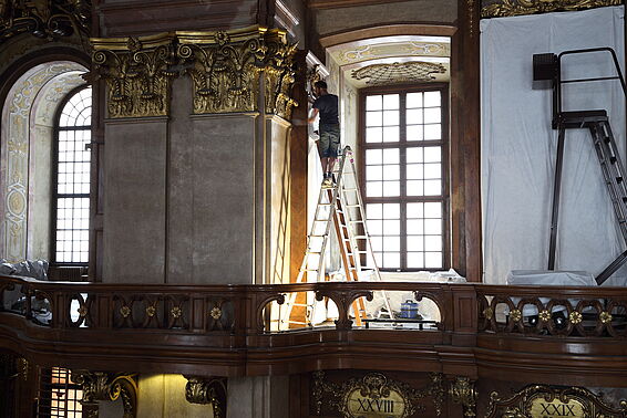 Mann auf der Leiter putzt die Holzwand.