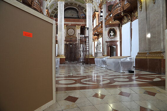 Holzkiste links lenkt den Blick auf die Leiter hinten im Saal.