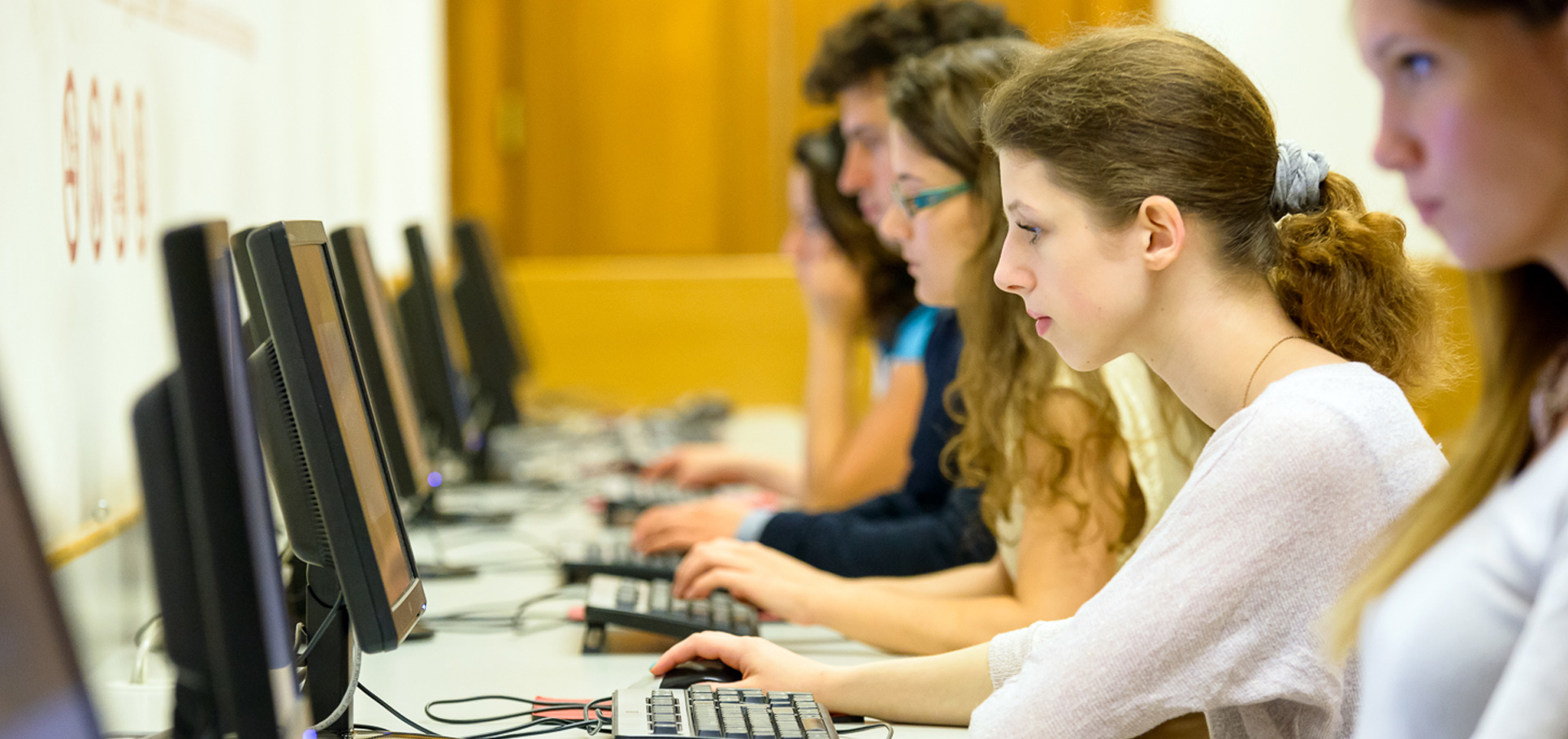 Junge Frauen und Männern sitzen nebeneinander vor Computern