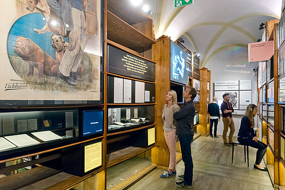 Verschiedene Menschen in Museumsraum mit Bücherregalen