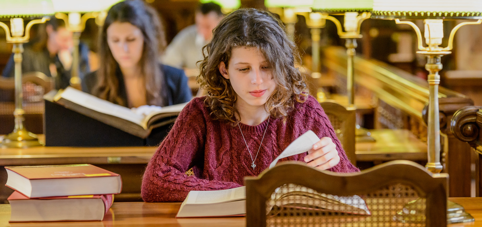 Junge Frauen sitzen in einem Lesesaal vor Büchern