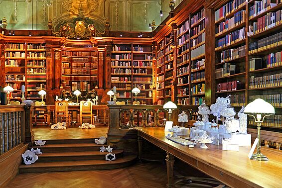 Foto von Saal mit Schreibtischen und edlen Bücherregalen, weiße Hochzeitsdeko auf den Tischen und am Boden