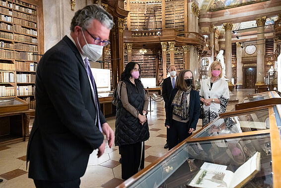 Fünf Personen in eleganter Kleidung stehen in einem Marmorsaal vor Vitrinen