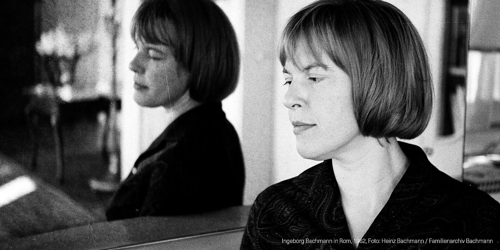 Schwarz-weißes Foto von Frau mit kurzen Haaren, die sich in Spiegel spiegelt.