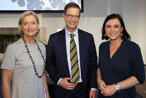 Eine blonde Frau links, ein Mann mit Brille in der Mitte und eine dunkelhaarige Frau rechts