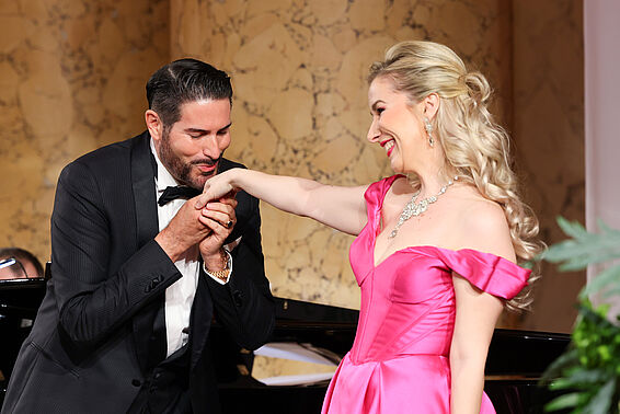 Ein Mann im Anzug küsst einer Frau im rosa Abendkleid die Hand