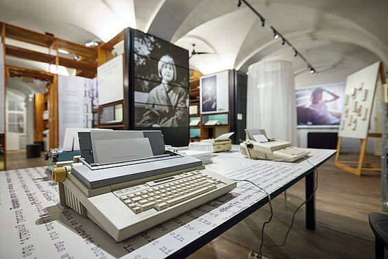 Museumsraum mit Regalen mit Fotografien, im Vordergrund eine Schreibmaschine..