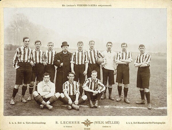 Schwarz-weißes Foto von Fußball-Mannschaft und ein Mann mit Bowler-Hut posieren auf Fußballfeld.