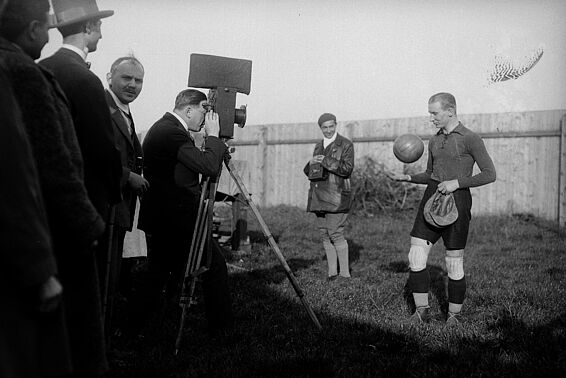 Mann mit großer Fachwerkkamera fotografiert Fußballer mit Ball in der Hand