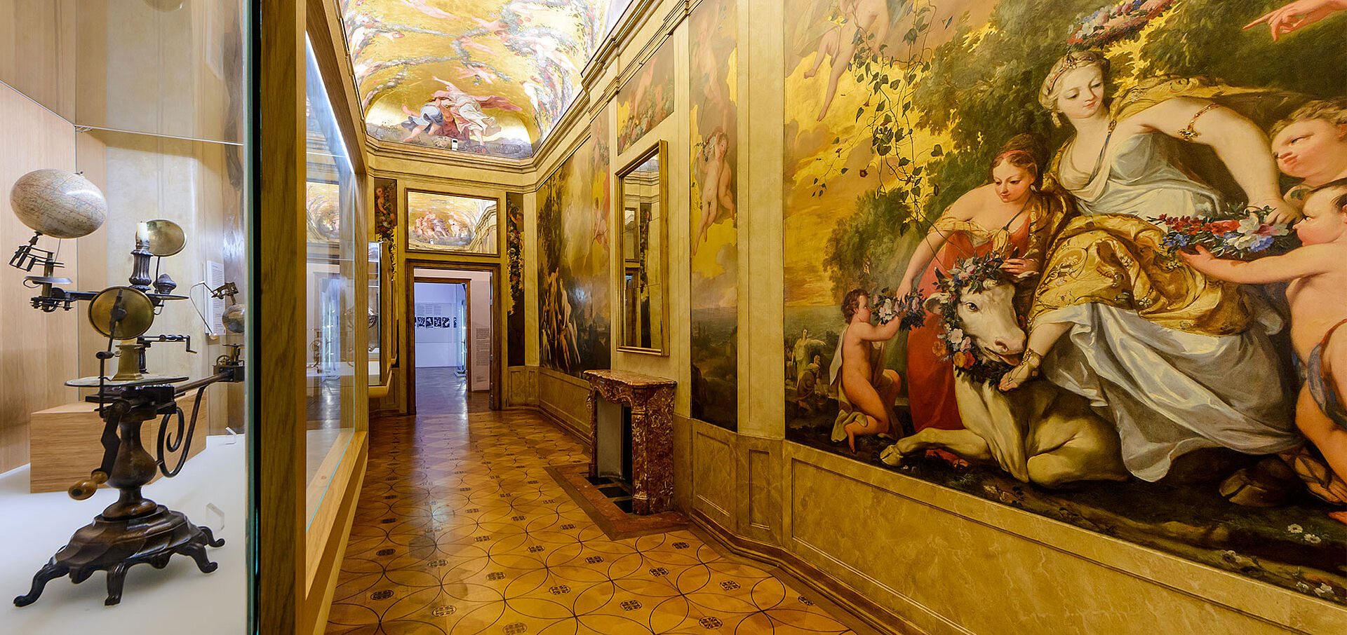 Foto von engem Raum mit Wandgemälden, Globen in Vitrinen und goldenen Wänden.