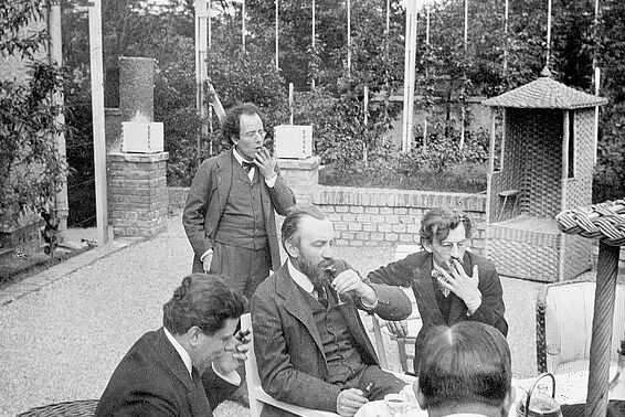 5 Männer in Anzügen sitzen auf einer Terrasse und rauchen