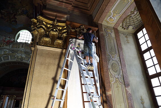 Arbeiter auf Leiter reinigt den Stuck.