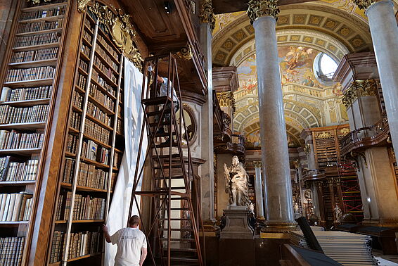 Zwei Personen befestigen weißes Papier an einem hohen Bücherregal