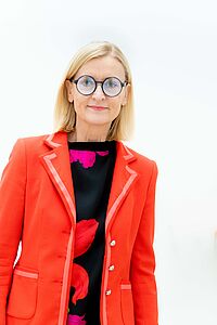 Foto von Frau mit rotem Blazer und Brille.