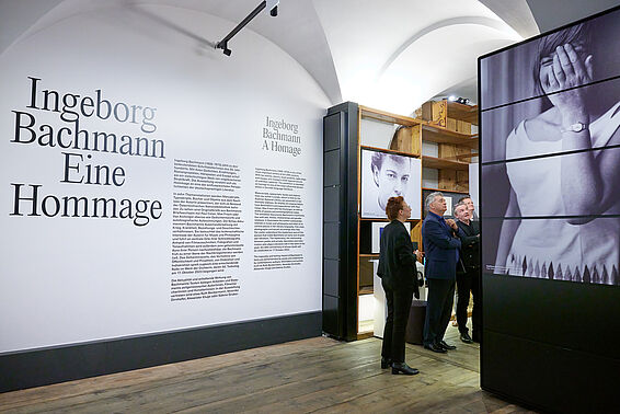 Foto von Museumsraum mit Titel der Ausstellung an der Wand und Regalen.