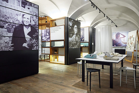 Museumsraum mit Regalen mit Fotografien, rechts ein Tisch mit Schreibmaschinen..