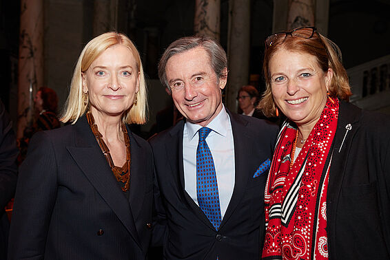 Zwei Frauen und ein Mann im Anzug posieren lächeln.