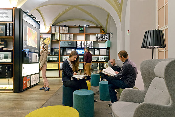 Verschiedene Menschen in Museumsraum mit Bücherregalen