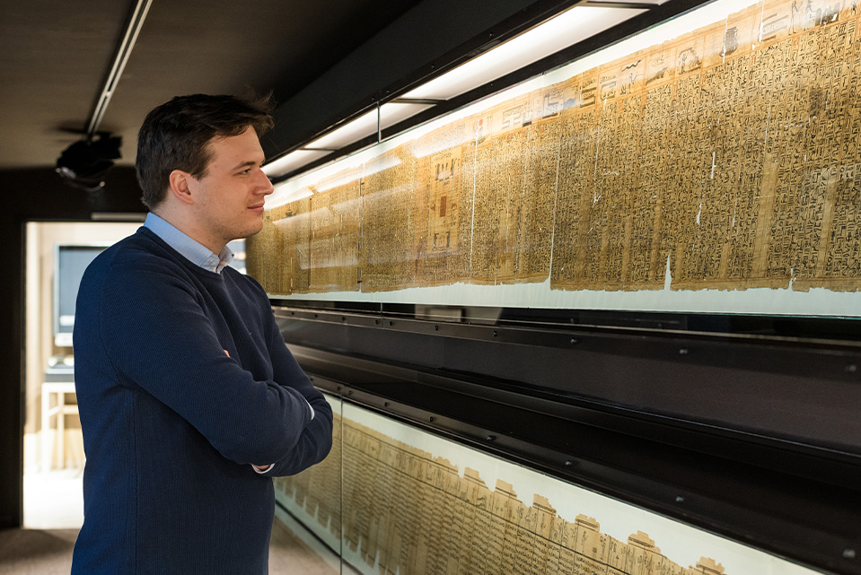 Ein Mann schaut sich eine Vitrine mit einem sehr langen Papyrus an