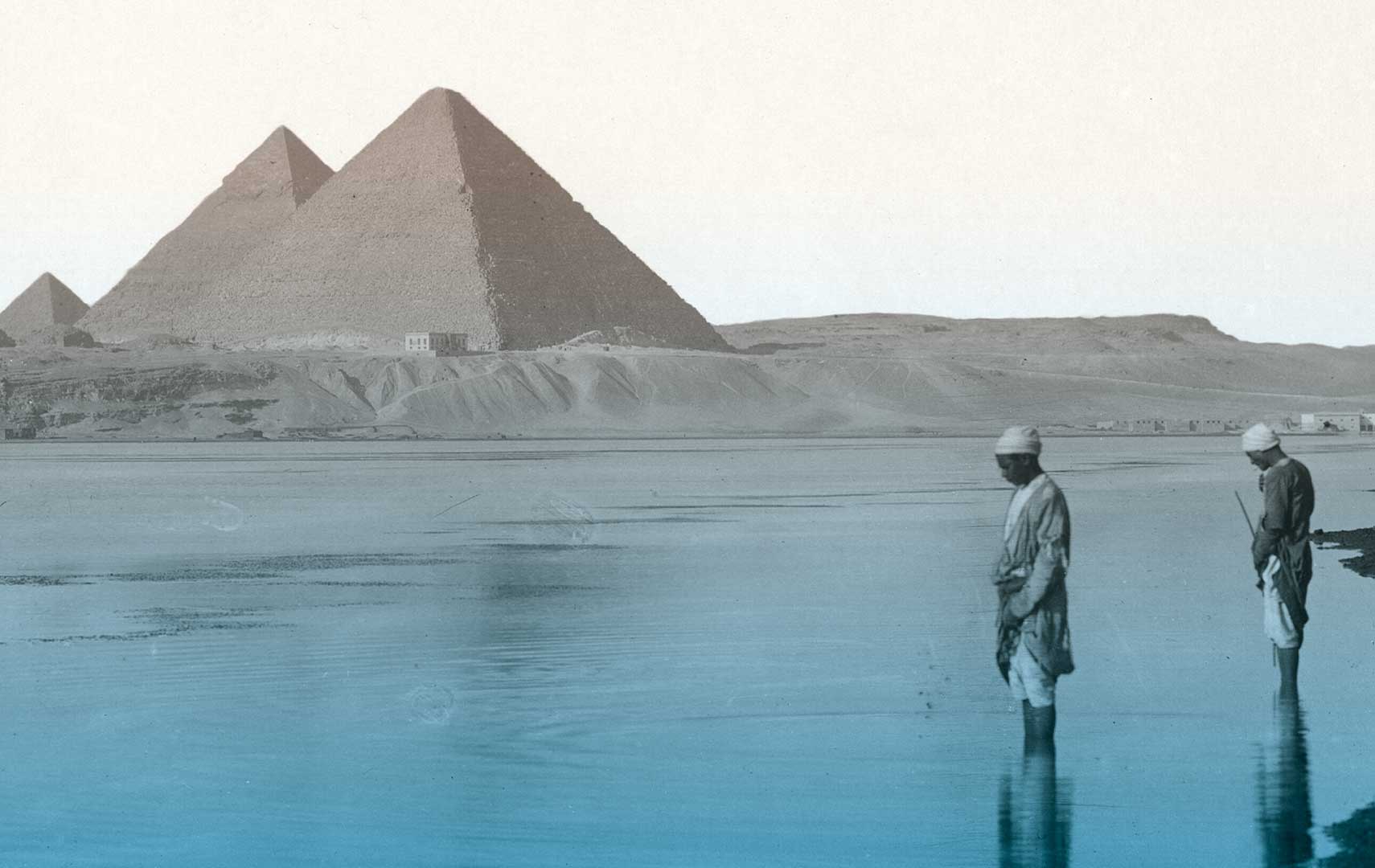Zwei Männer stehen in einem Fluss vor den Pyramiden