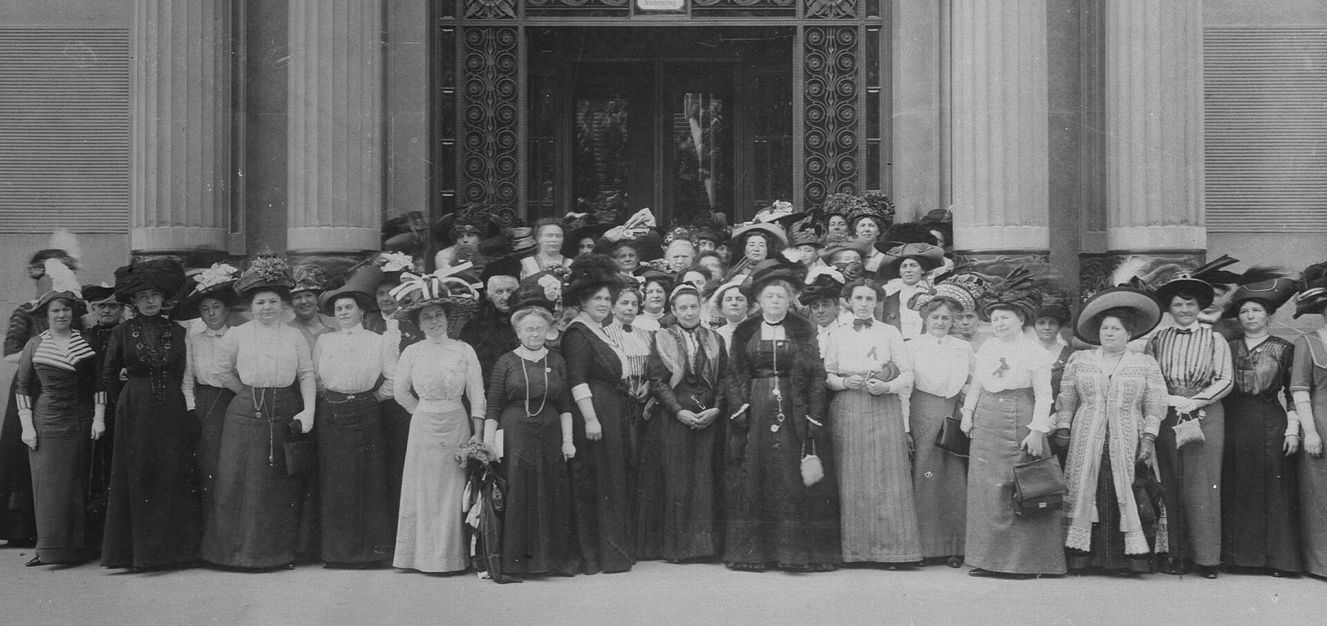 Schwarz-weiß Aufnahme, Elegant gekleidete Damen mit Hüten, Generalversammlung des Bundes Österreichischer Frauenvereine am 13. Mai 1911 vor dem Portal der Handelskammer in Wien, Stubenring 8-10. 