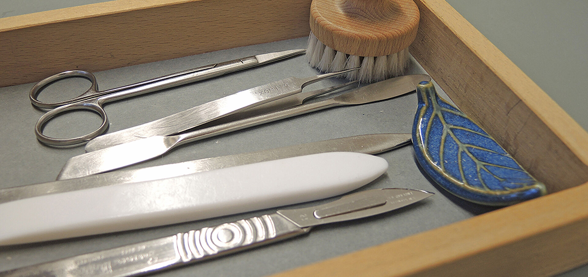 Schere, Pinzette, Messer, Bürste und andere Restaurier-Werkzeuge in einer Holzbox
