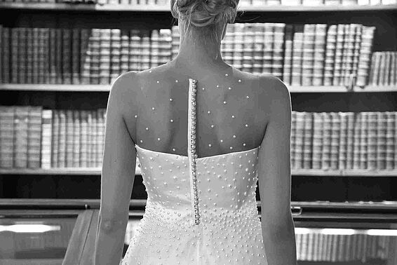 Schwarz-weißes Foto von Frau in weißem Kleid vor einem vollen Bücherregal