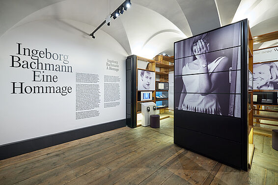 Museumsraum mit Text an der Wand und Regalen mit Fotografien.