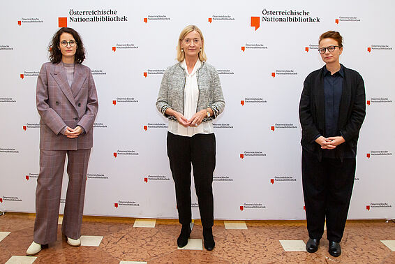 Drei Frauen vor einer Logowand der Österreichischen Nationalbibliothek 