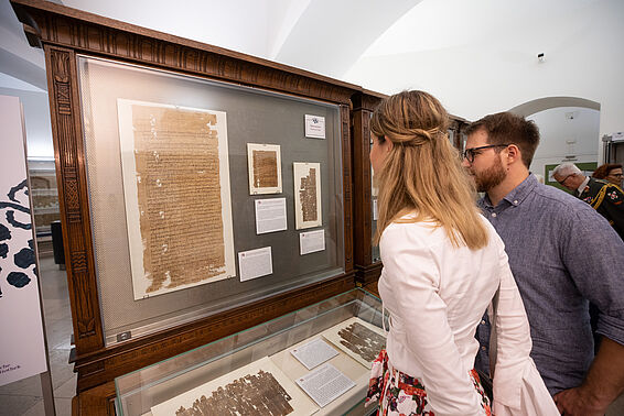 Eine blonde Frau und ein bärtiger Mann mit Brille sehen sich eine Vitrine im Papyrusmuseum an