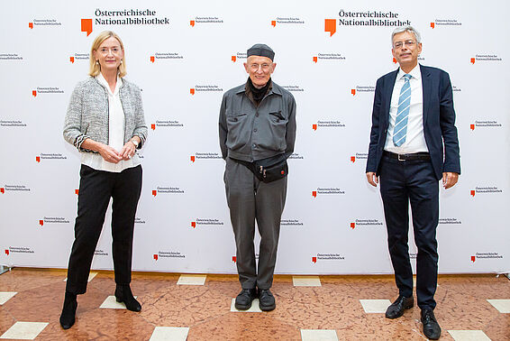 Zwei Männer und eine Frau vor einer Logowand der Österreichischen Nationalbibliothek 
