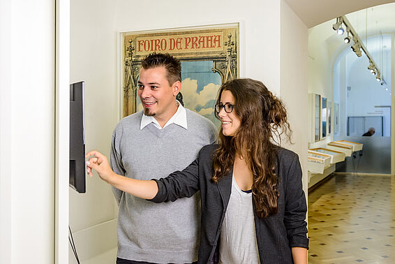 Ein Mann und eine Frau bedienen einen Touchscreen in einem Museumsraum
