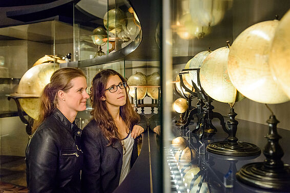 Zwei Frauen betrachten Globen in einer Glasvitrine