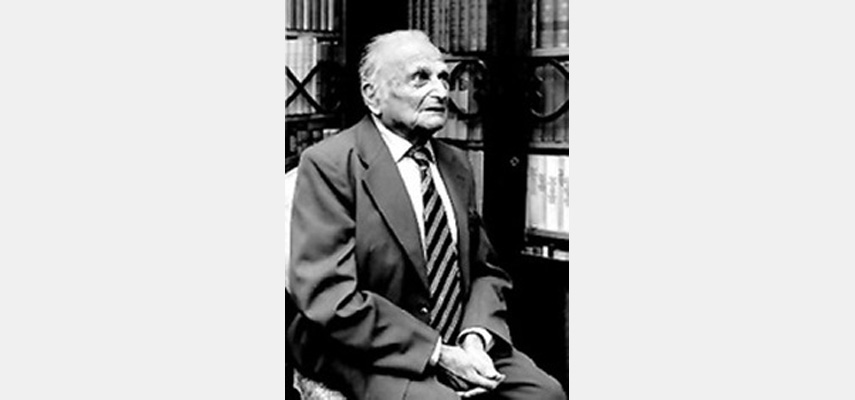 Mann sitzt vor Bücherregal, Hände gefaltet, Blick nach oben rechts, schwarz-weiß
