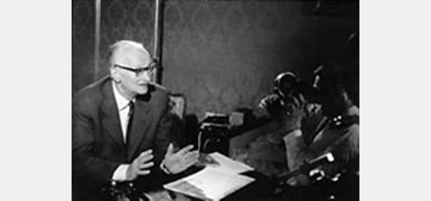 Mann im Anzug hält Rede vor Kameras, schwarz-weiß