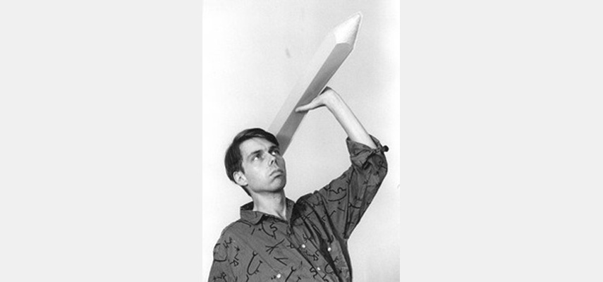 Mann mit gemustertem Hemd hält übergroßen Bleistift, als wolle er ihn werfen, schwarz-weiß